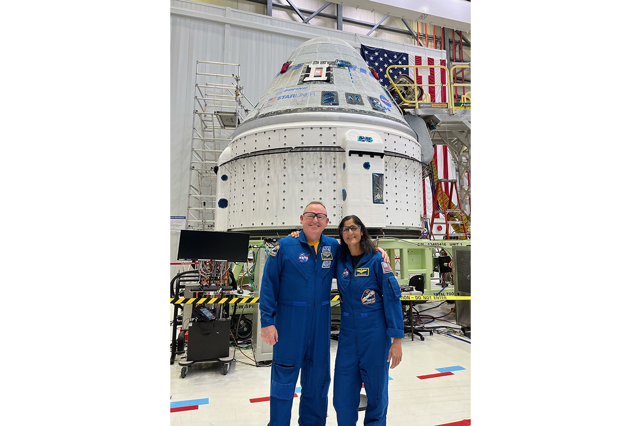NASA astronauts Butch Wilmore and Suni Williams in front of the Crew Flight Test spacecraft in the Commercial Crew and Cargo Processing Facility at Kennedy Space Center in Florida.