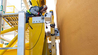 Technician on test stand adjusts equipment next to orange rocket core stage.